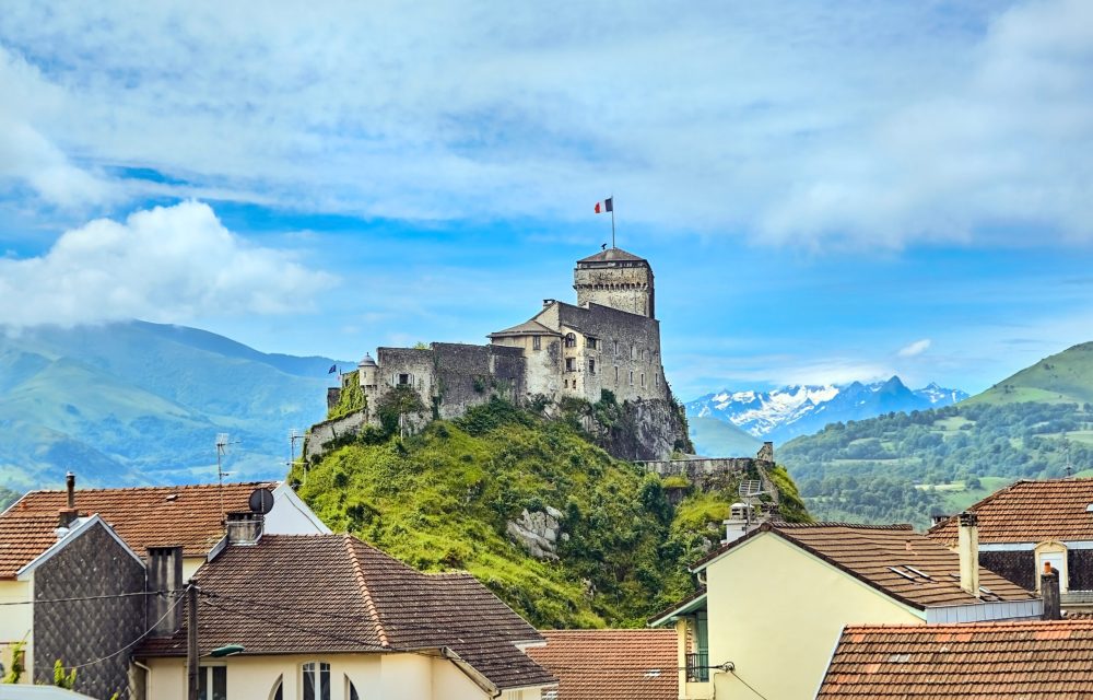 Chateau Fort of Lourdes. Castle on a rock. Snowy mountain peaks. Blue sky with white clouds. City in the Hautes-Pyrénées, France